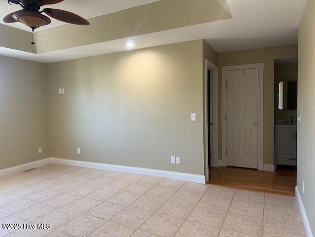 unfurnished room with ceiling fan, light tile patterned flooring, and a raised ceiling