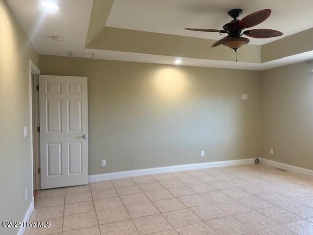 spare room with ceiling fan, a raised ceiling, and light tile patterned floors