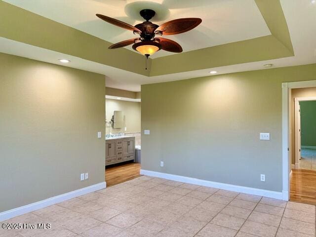 unfurnished bedroom with ensuite bath, a raised ceiling, ceiling fan, and light tile patterned flooring