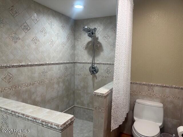 bathroom with tiled shower, toilet, and tile walls