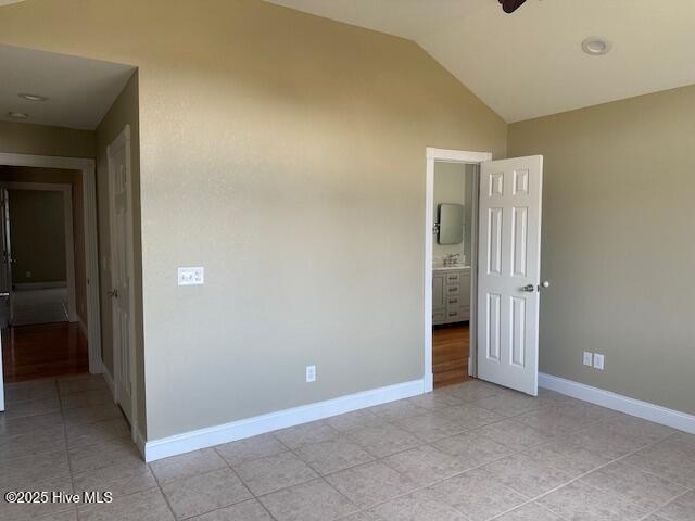 unfurnished bedroom with ensuite bathroom, light tile patterned flooring, and vaulted ceiling