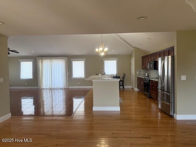 kitchen with lofted ceiling, decorative backsplash, an island with sink, dark brown cabinetry, and stainless steel appliances