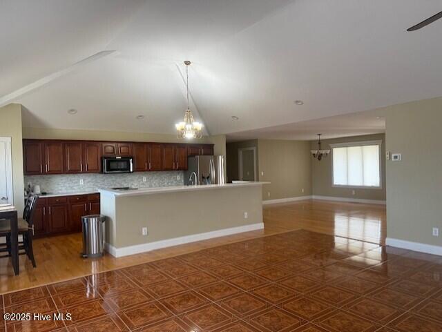 kitchen featuring decorative backsplash, appliances with stainless steel finishes, a kitchen bar, vaulted ceiling, and an island with sink