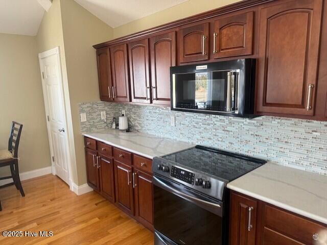 kitchen with lofted ceiling, decorative backsplash, light stone countertops, stainless steel electric range oven, and light hardwood / wood-style floors