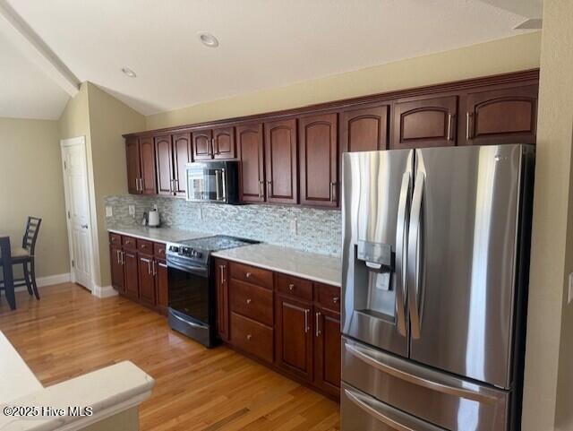 kitchen with light hardwood / wood-style floors, backsplash, appliances with stainless steel finishes, and vaulted ceiling