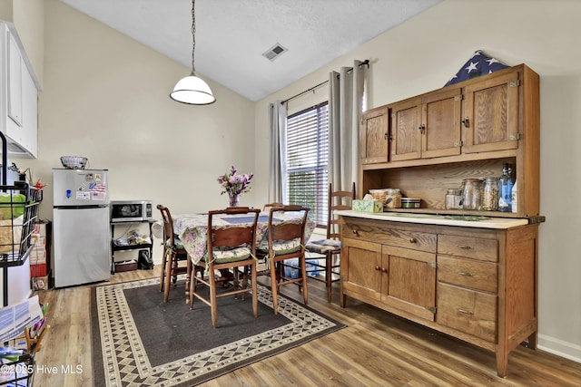 dining space with wood-type flooring, a textured ceiling, and vaulted ceiling