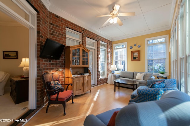 living room featuring light hardwood / wood-style floors, ceiling fan, ornamental molding, and brick wall