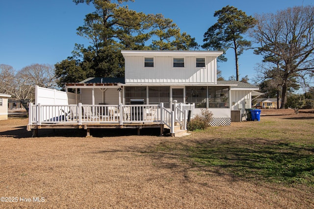 rear view of house featuring a lawn, a wooden deck, and a sunroom