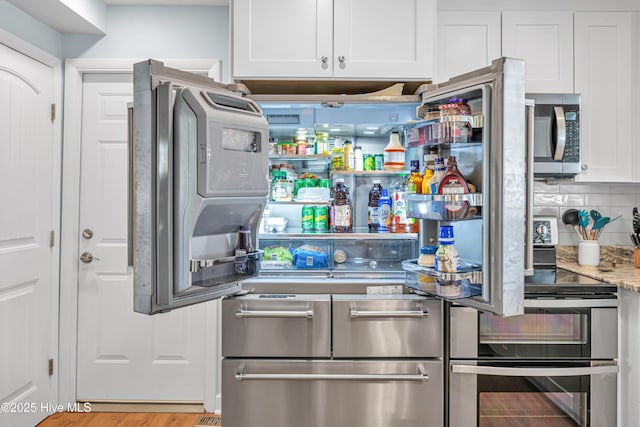 kitchen featuring appliances with stainless steel finishes, white cabinetry, backsplash, and light stone countertops