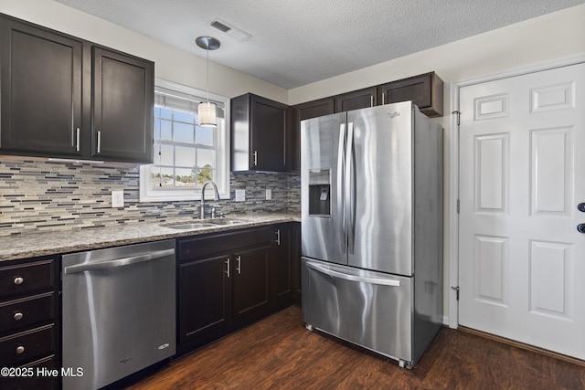 kitchen featuring sink, hanging light fixtures, dark wood-type flooring, stainless steel appliances, and light stone counters