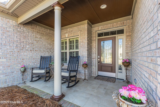 view of exterior entry featuring brick siding and a porch