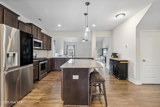 kitchen featuring a kitchen bar, hardwood / wood-style floors, tasteful backsplash, kitchen peninsula, and appliances with stainless steel finishes