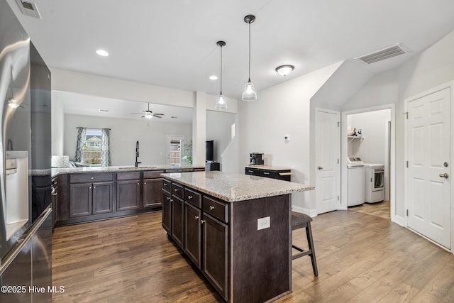 kitchen featuring a kitchen breakfast bar, independent washer and dryer, stainless steel refrigerator, a kitchen island, and decorative light fixtures