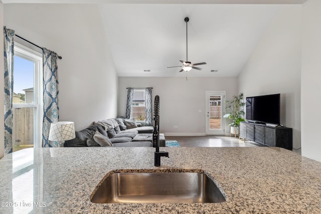 kitchen with vaulted ceiling, wood-type flooring, light stone countertops, ceiling fan, and sink