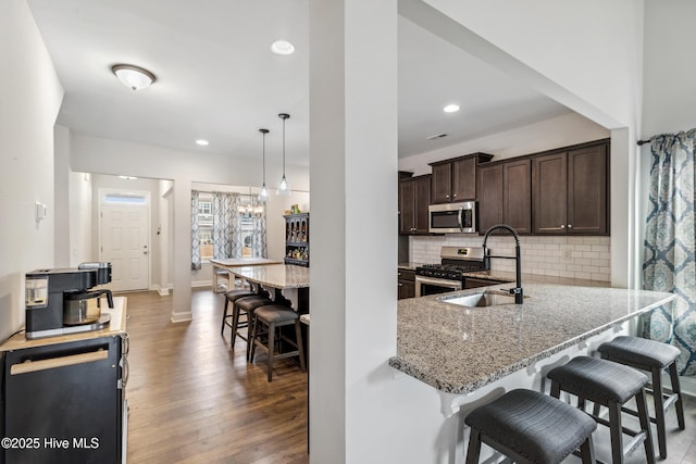 kitchen featuring a breakfast bar area, appliances with stainless steel finishes, hanging light fixtures, kitchen peninsula, and light stone countertops