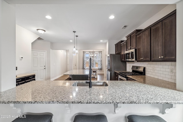 kitchen featuring stainless steel appliances, a kitchen bar, light stone counters, sink, and decorative light fixtures