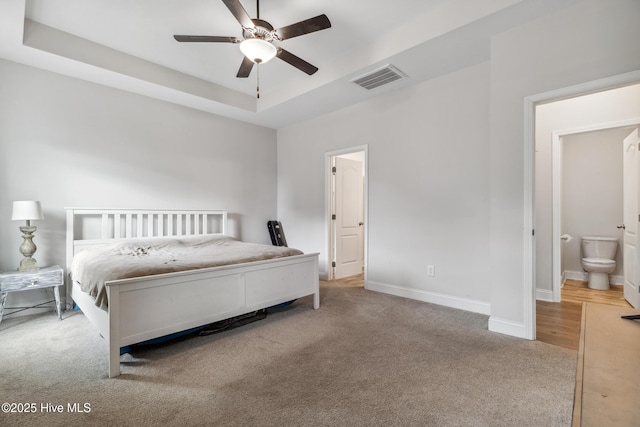 bedroom featuring ensuite bathroom, a raised ceiling, ceiling fan, and light colored carpet