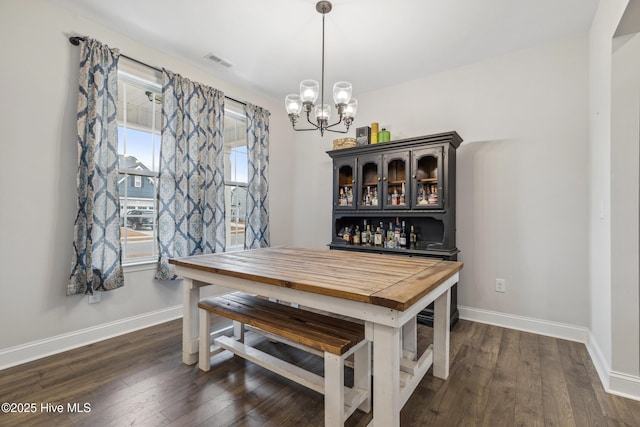 dining space with dark wood-type flooring, a chandelier, and bar