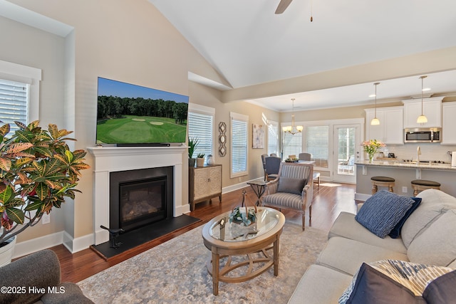 living room featuring ceiling fan with notable chandelier, high vaulted ceiling, and dark wood-type flooring