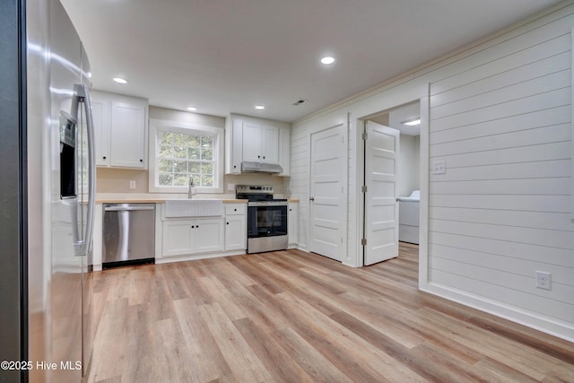 kitchen featuring appliances with stainless steel finishes, light wood-type flooring, sink, white cabinets, and wood walls