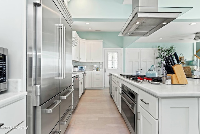 kitchen featuring light wood-type flooring, stainless steel appliances, white cabinets, a kitchen island, and range hood