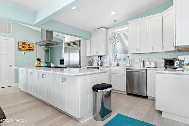 kitchen with white cabinets, hanging light fixtures, a kitchen island, stainless steel appliances, and extractor fan