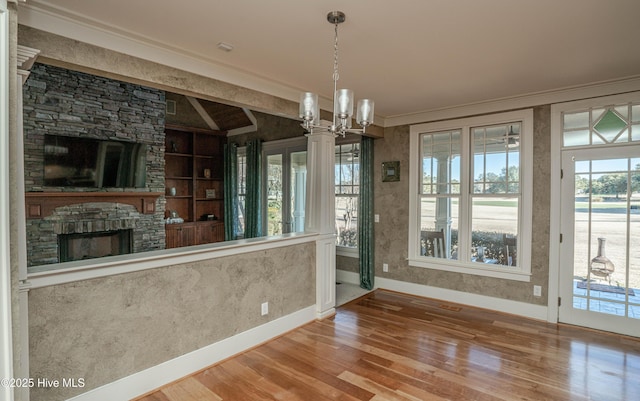 interior space with crown molding, built in features, hardwood / wood-style floors, and a stone fireplace