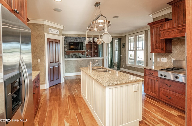 kitchen with decorative light fixtures, sink, light wood-type flooring, appliances with stainless steel finishes, and an island with sink