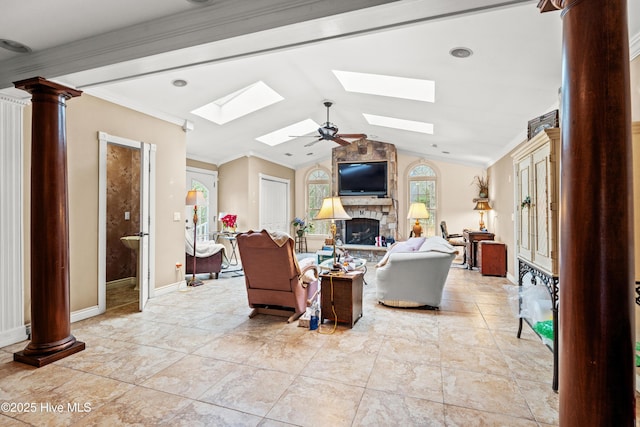 living room featuring ceiling fan, lofted ceiling with skylight, a stone fireplace, and decorative columns