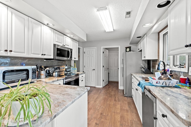 kitchen featuring backsplash, light stone countertops, appliances with stainless steel finishes, a textured ceiling, and white cabinets