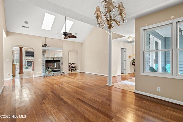 unfurnished living room with a fireplace, a wealth of natural light, ceiling fan with notable chandelier, and decorative columns