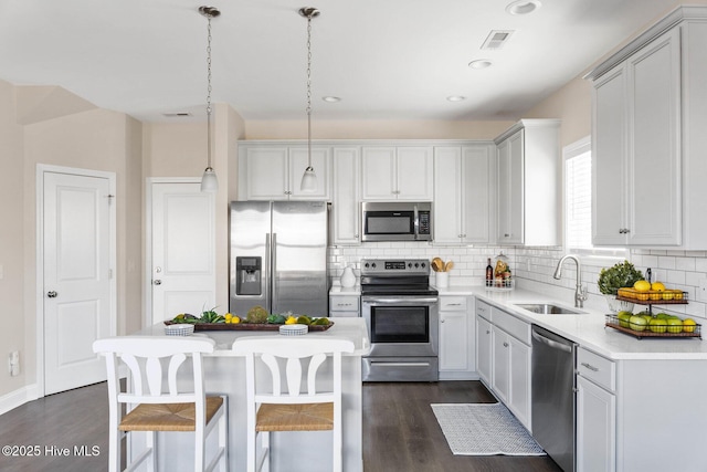 kitchen with a kitchen island, appliances with stainless steel finishes, sink, decorative backsplash, and hanging light fixtures