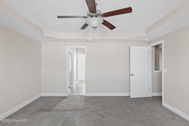 spare room with ceiling fan, light colored carpet, and a tray ceiling