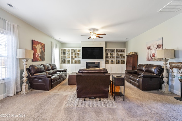 carpeted living room with built in shelves, a fireplace, and ceiling fan