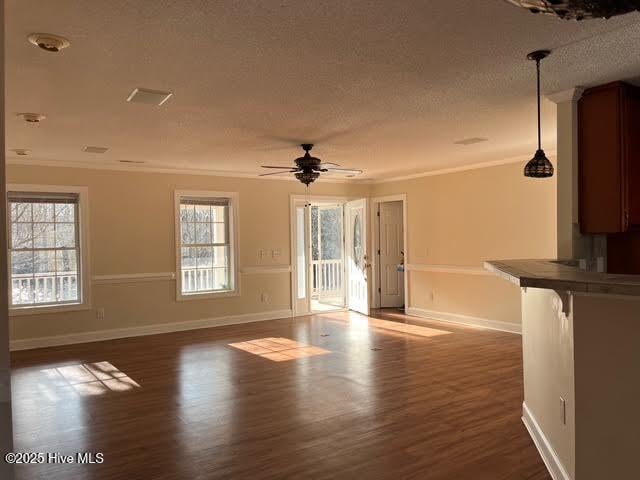 unfurnished living room featuring dark wood-style floors, a textured ceiling, baseboards, and crown molding