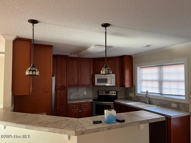 kitchen featuring white microwave, a peninsula, a sink, stainless steel electric range, and pendant lighting