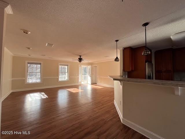 unfurnished living room with a textured ceiling, dark wood finished floors, a ceiling fan, and baseboards