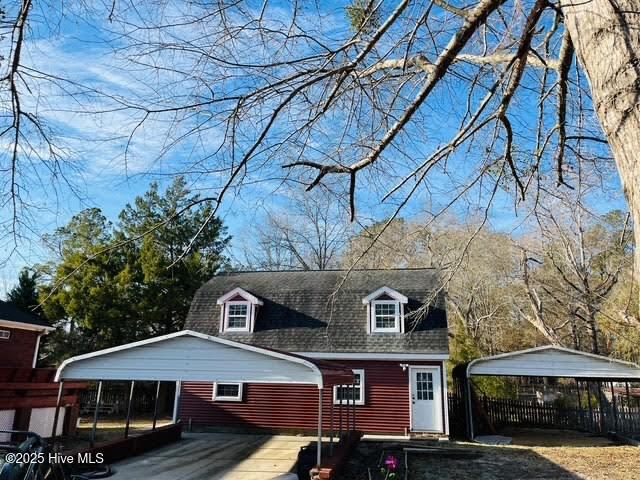 view of front facade featuring a detached carport, roof with shingles, driveway, and fence