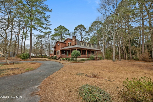 view of front facade with driveway, a chimney, and covered porch