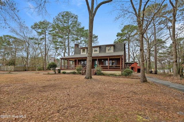 back of house featuring a chimney, fence, a porch, and a shingled roof
