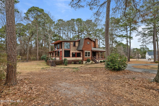 back of property with a gambrel roof, a chimney, and covered porch