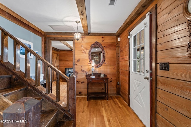 foyer featuring beam ceiling, visible vents, light wood-style floors, stairs, and wooden walls