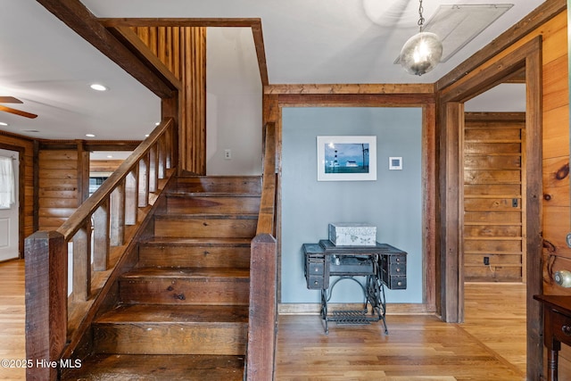 staircase featuring wood-type flooring, log walls, and ceiling fan