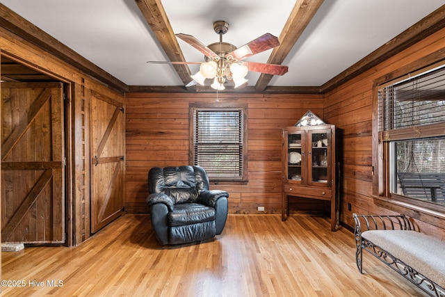 sitting room with light wood-style floors, beam ceiling, wood walls, and a ceiling fan