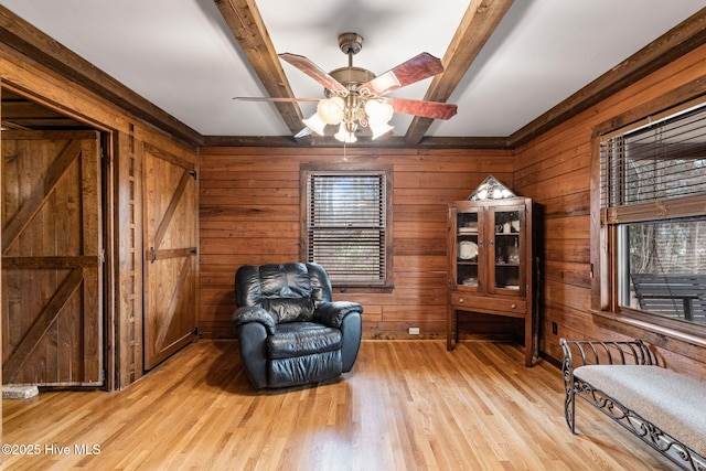 living area featuring ceiling fan, light hardwood / wood-style flooring, beamed ceiling, and wood walls