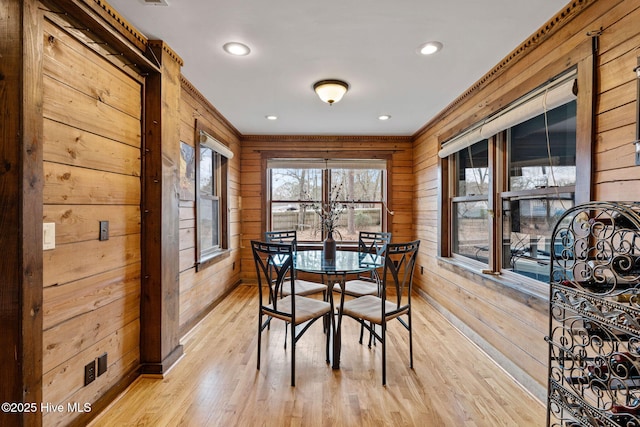 dining room featuring wood walls, ornamental molding, and light wood-type flooring