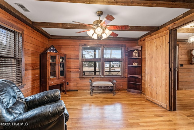 sitting room with ceiling fan, wood walls, beam ceiling, and light wood-type flooring