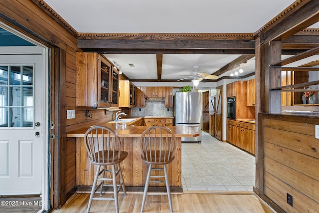 kitchen featuring a peninsula, a sink, freestanding refrigerator, brown cabinetry, and black oven