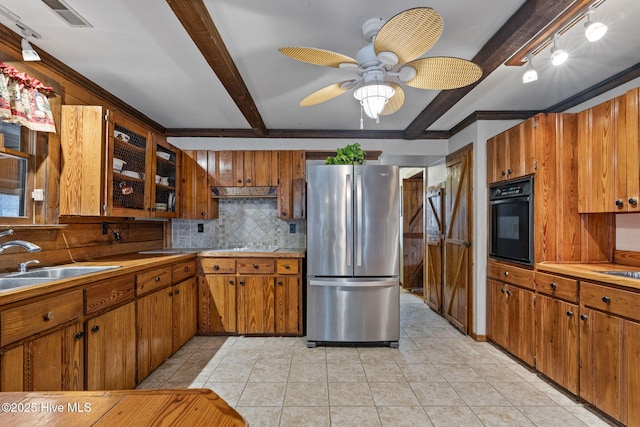kitchen featuring a sink, brown cabinets, black oven, beam ceiling, and freestanding refrigerator