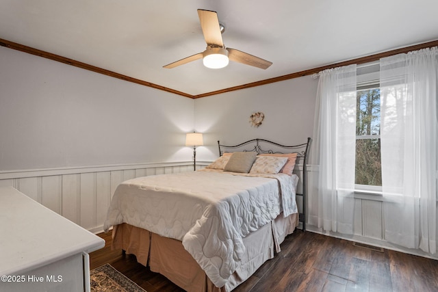 bedroom with crown molding, wainscoting, ceiling fan, dark wood-style flooring, and visible vents